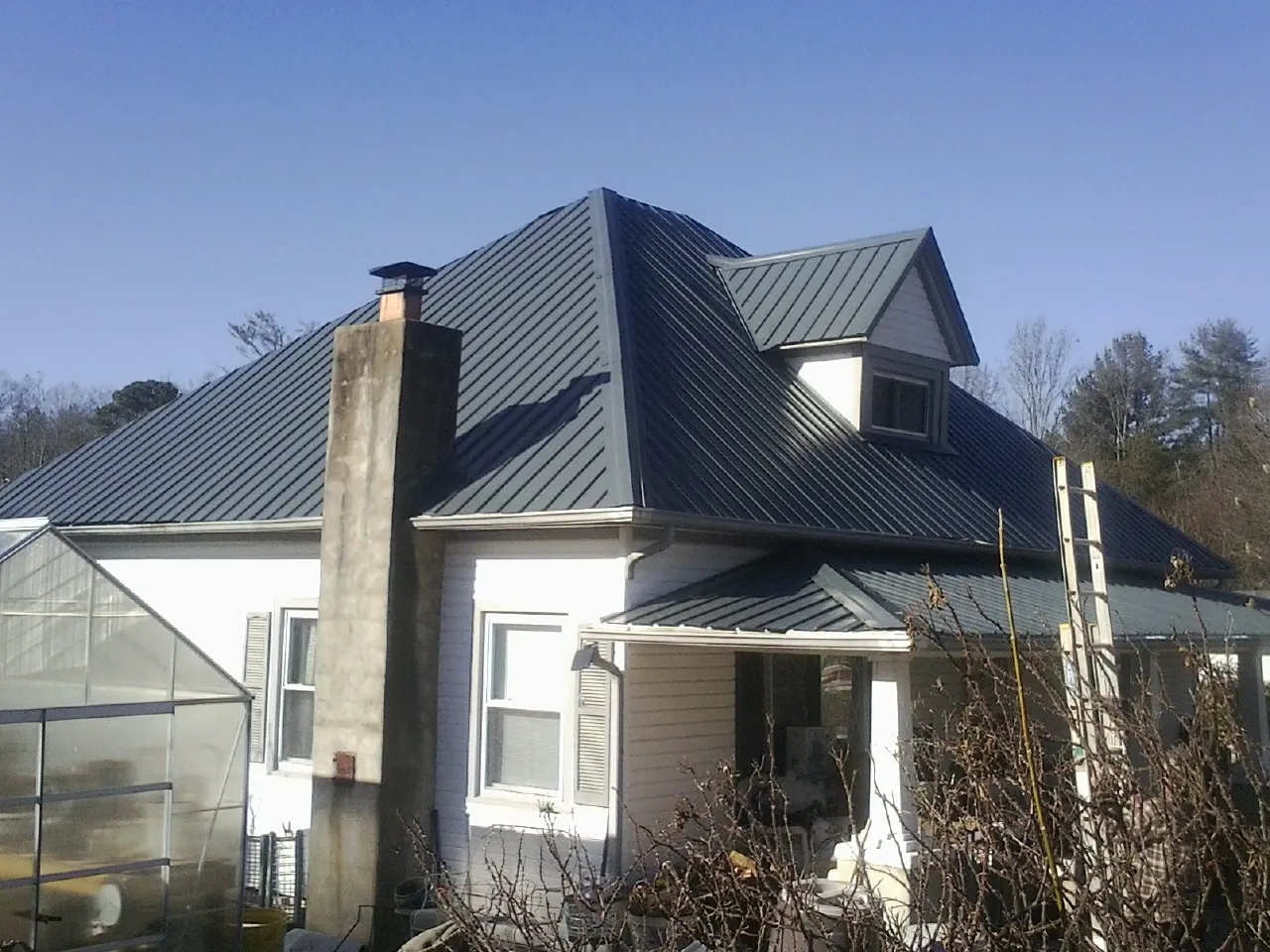 Dark blue standing seam metal roof on a white farmhouse with dormer — Slate & Tile Roof Repair by Roofing Brothers in Buffalo Creek