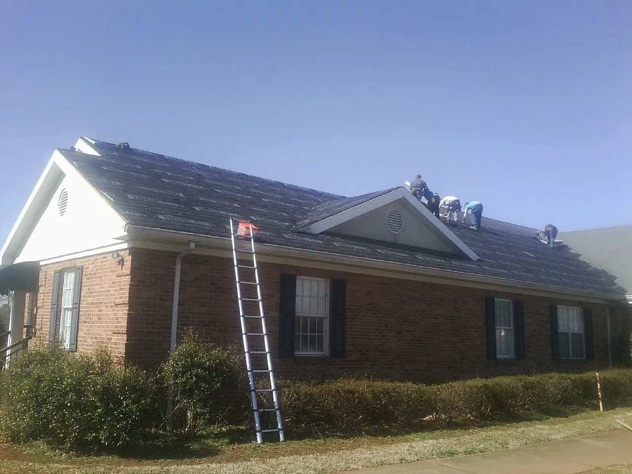 Crew tearing shingles off a brick ranch roof with a ladder set — Emergency Roof Repair work by our crew in Buffalo Creek