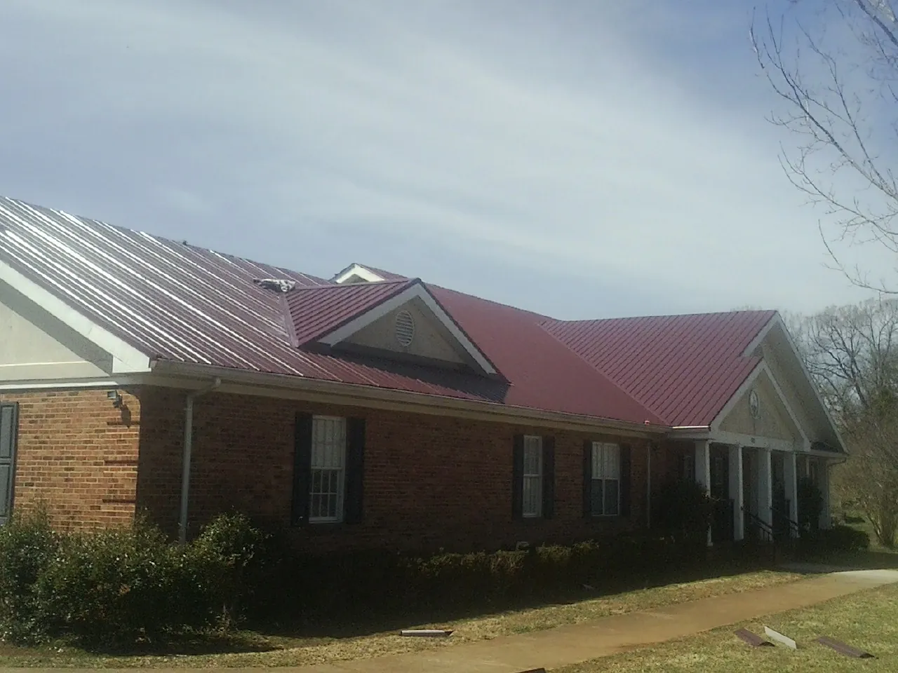Red metal roof with gabled entries on a long brick building, from a Hail Damage Roof Repair job in Buffalo Creek