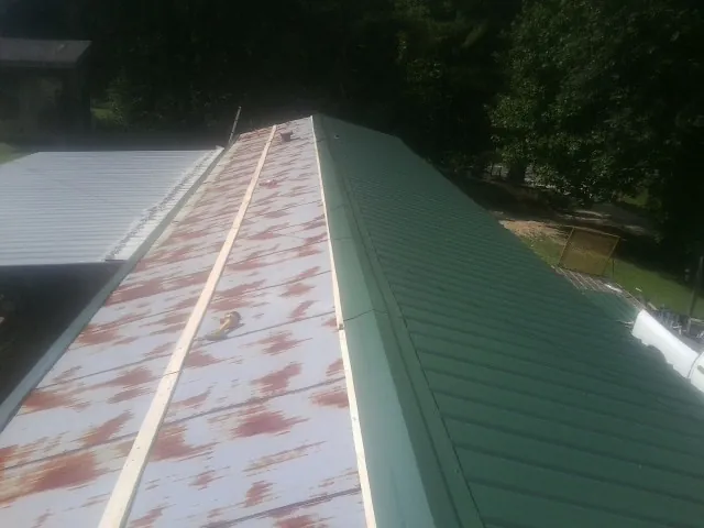 Old rusted panels beside newly installed green metal roofing — Wind Damage Roof Repair by Roofing Brothers in Buffalo Creek