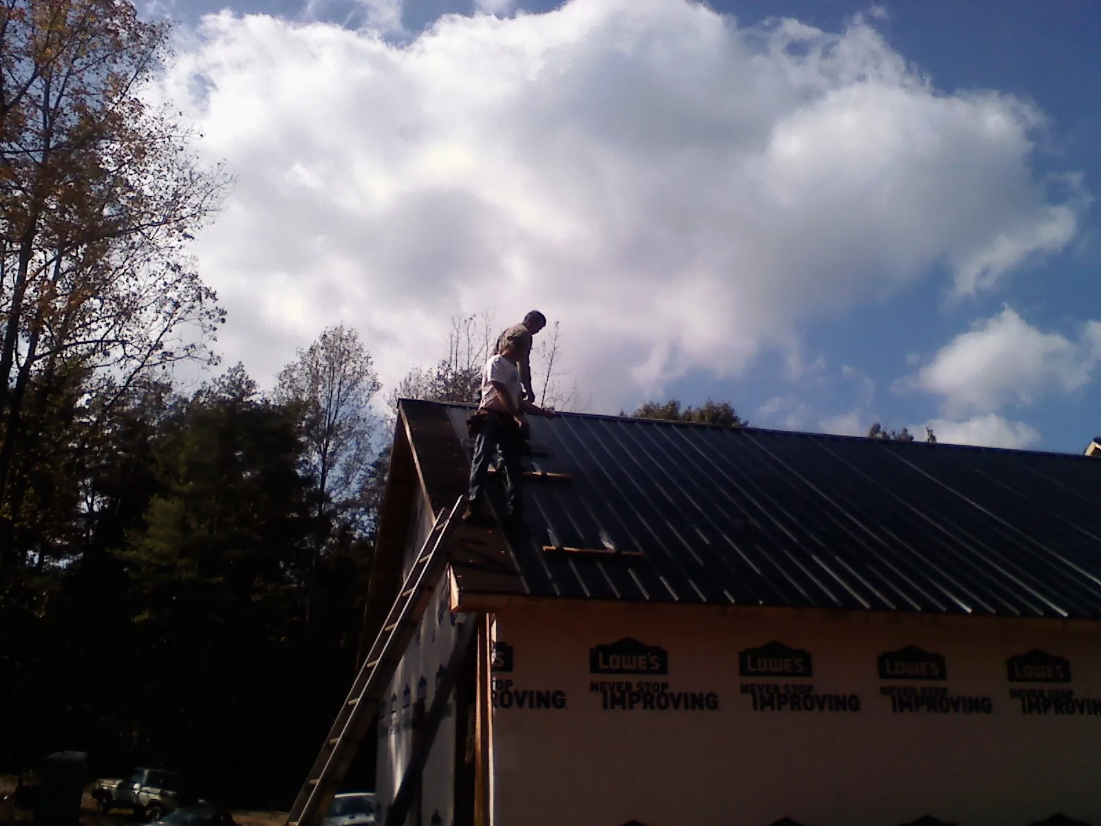 Roofer fastening dark metal panels high against a cloudy sky, from a Roof Inspection job in Buffalo Creek