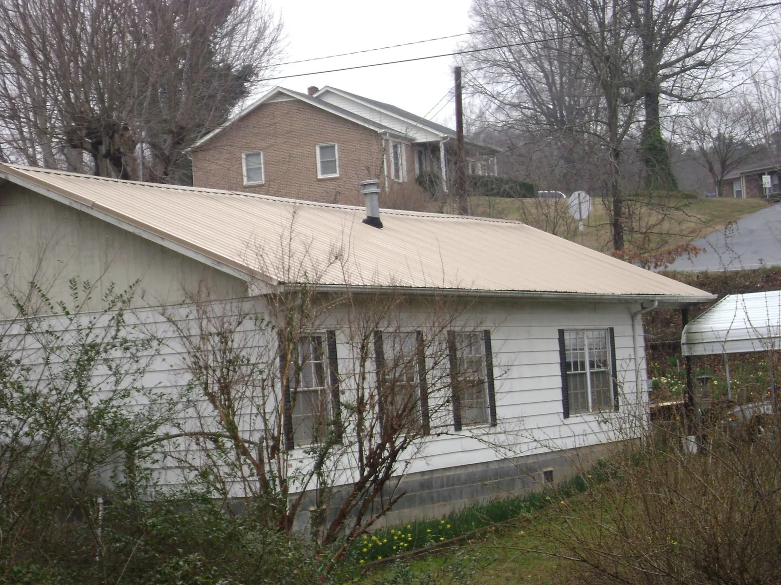 Tan metal roof on a white sided house set into a hillside — Commercial Roofing by Roofing Brothers in Buffalo Creek