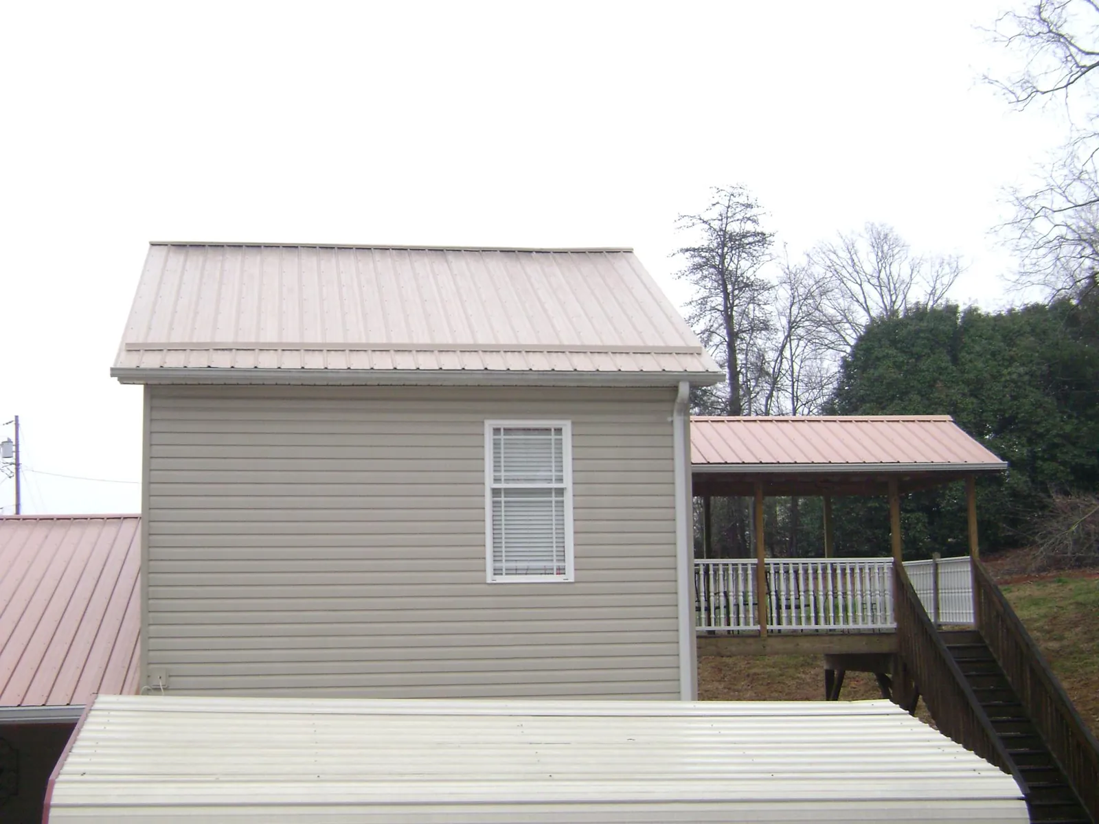 Tan metal roofs on a two story addition and attached porch, from a Roof Replacement job in Buffalo Creek